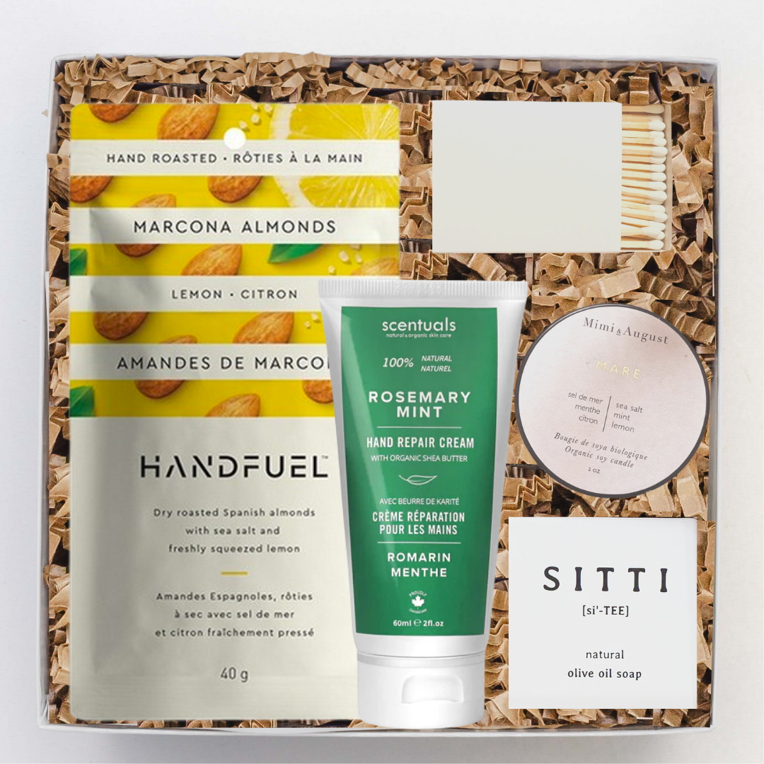 A gift box containing various self-care products including a candle, almonds, soap, hand cream, and a satin ribbon.